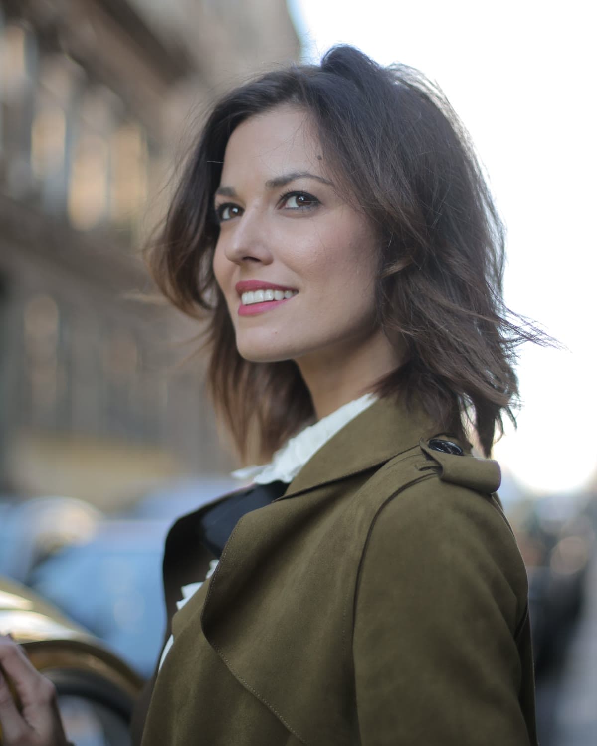 A woman in an olive jacket looking back on a softly lit city street